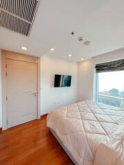 Modern bedroom with wooden floor, large window, and mounted television