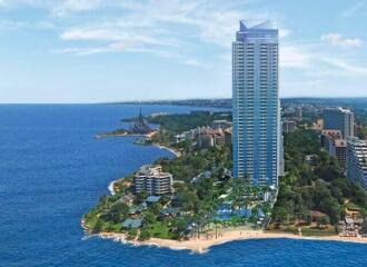 Aerial view of a high-rise residential building near a beach with surrounding greenery