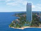 Aerial view of a high-rise residential building near a beach with surrounding greenery