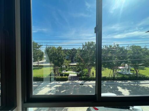 View from a building window overlooking a sunny neighborhood with trees and a clear blue sky