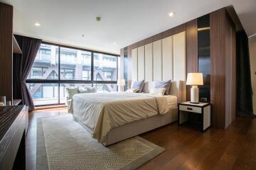 Modern bedroom with a large bed, floor-to-ceiling windows, and wooden accents