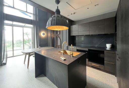 Modern kitchen with dark cabinetry and marble island under a large pendant light