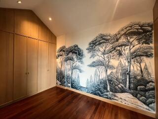 Spacious bedroom with artistic forest-themed wallpaper and hardwood floor