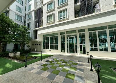 Front entrance of a modern apartment building with checkered tiles and green lawn