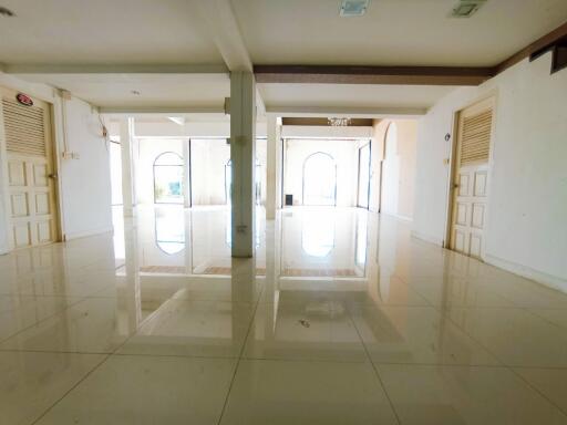 Spacious and brightly lit empty living space with glossy tiled flooring and multiple doors