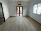Spacious empty room with wooden flooring, white walls, and large windows