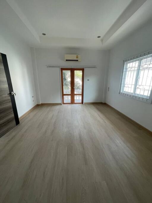 Spacious empty room with wooden flooring, white walls, and large windows