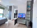 Compact bedroom with open wardrobe and mounted TV