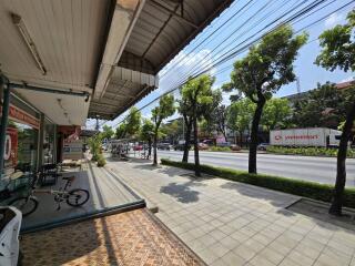 View of the street from a covered sidewalk with shops on one side and a road with visible traffic