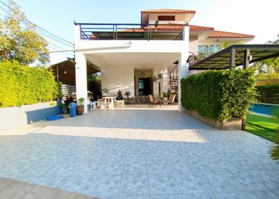 Spacious exterior with tiled patio, two-story home with balcony and lush green surroundings