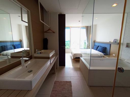 Spacious modern bathroom with double vanity and glass shower enclosure extending to a bedroom view