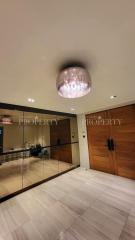 Elegant entrance hall with modern chandelier, mirrored walls, and wooden doors