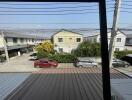 Residential neighborhood view from a window showing houses and parked cars under a clear sky