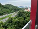 Scenic view from a high-rise apartment balcony overlooking a lush green area and cityscape