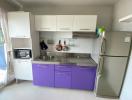 Modern kitchen with white and purple cabinets, stainless steel sink, microwave, and a refrigerator