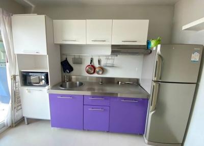 Modern kitchen with white and purple cabinets, stainless steel sink, microwave, and a refrigerator