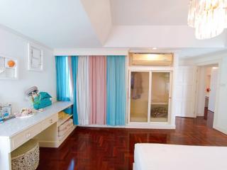 Spacious bedroom with hardwood floors, large window with colorful curtains, and built-in wardrobe