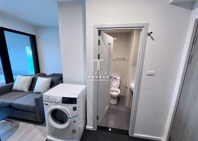 Modern apartment interior showing a combination of living room with a grey sofa and a bathroom entrance with a white door