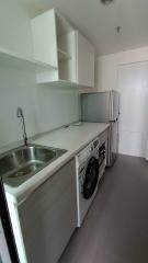 Compact kitchen with white cabinetry, stainless steel sink, and appliances including a refrigerator and washing machine