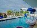 Residential outdoor swimming pool with water slide and patio furniture under a clear sky