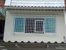 Two-story residential building exterior with a white tiled roof and protected windows