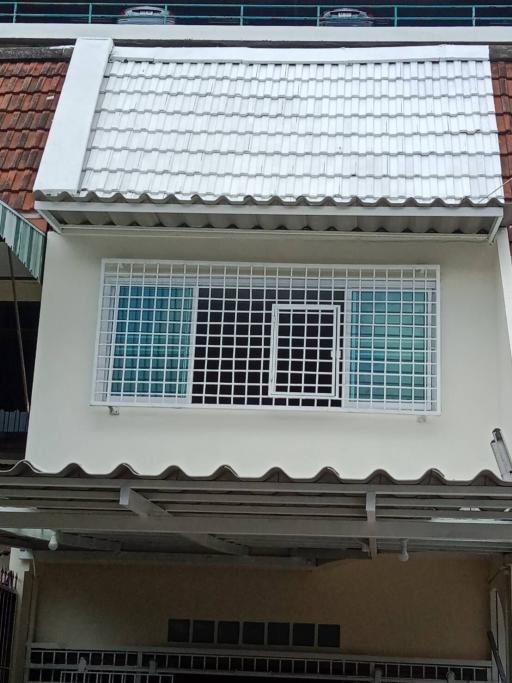 Two-story residential building exterior with a white tiled roof and protected windows