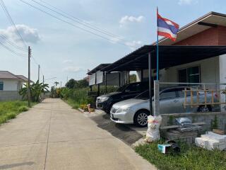 Street view of a residential property with parked cars and a Thailand flag