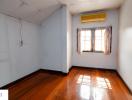 Empty bedroom with wooden floor, window, and air conditioning unit