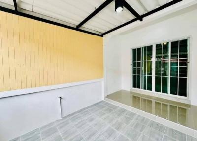 Bright empty room with yellow accent wall, large window, and tiled flooring