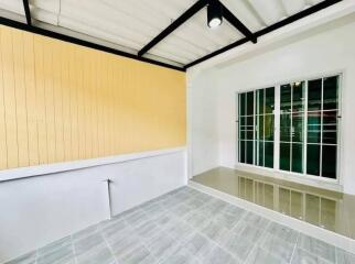 Bright empty room with yellow accent wall, large window, and tiled flooring