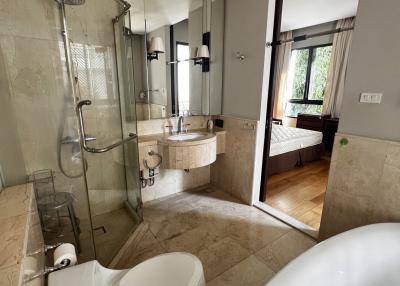 Elegant bathroom with a shower and marble tiles leading to a bedroom view