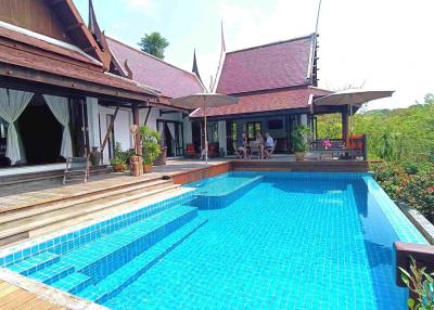 Spacious outdoor pool area with wooden deck and traditional house in the background