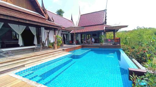 Spacious outdoor pool area with wooden deck and traditional house in the background