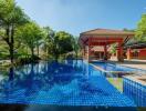Luxurious outdoor swimming pool with adjacent covered patio area surrounded by lush greenery