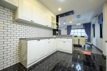 Modern kitchen with white cabinetry and black marble flooring connected to a vibrant living space