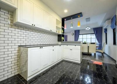 Modern kitchen with white cabinetry and black marble flooring connected to a vibrant living space