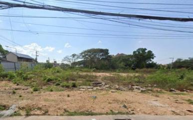 Empty residential plot with surrounding vegetation under a clear sky