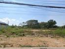 Empty residential plot with surrounding vegetation under a clear sky