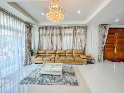 Spacious and well-lit living room with large sofa, elegant curtains, and chandelier