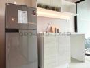 Modern compact kitchen with stainless steel refrigerator, white cabinetry, and stylish backsplash