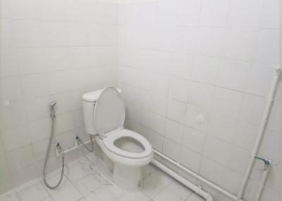 Neat white tiled bathroom with toilet and hand-held shower