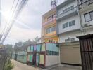 Colorful multi-story residential building exterior with a garage and surrounded by a metal fence