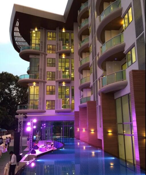 Modern apartment building with illuminated balcony features and pool area during twilight