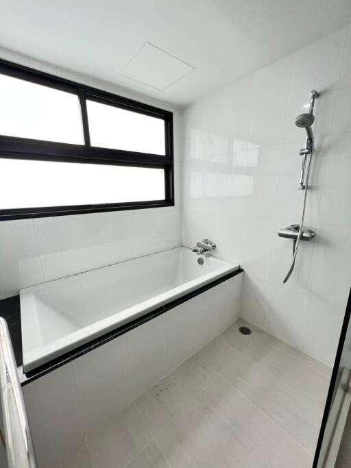 Modern bathroom interior with a clean bathtub, handheld showerhead, and large window