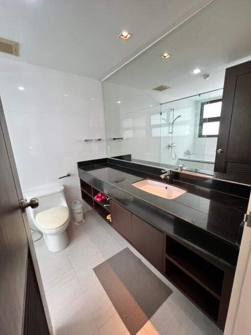 Modern bathroom interior with glass shower, large mirror, and dark wood vanity