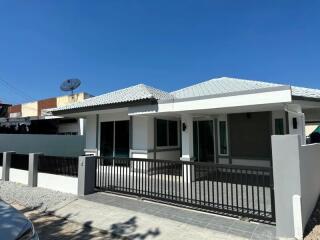 Single-story residential home with grey roofing and fenced front patio under a clear blue sky