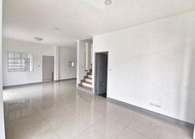 Spacious and well-lit empty living space with glossy tiled flooring, stair access, and neutral color scheme