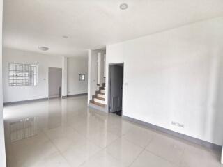 Spacious and well-lit empty living space with glossy tiled flooring, stair access, and neutral color scheme