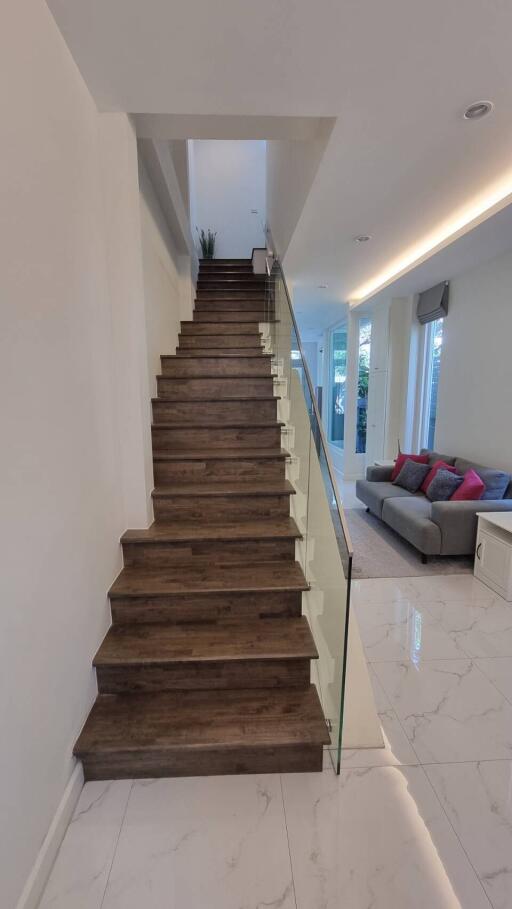 Modern staircase with glass railing, wooden steps, and polished floor leading to the upper level of a home