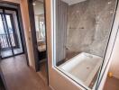 Modern bathroom with marble walls, glass shower enclosure, and direct access to balcony